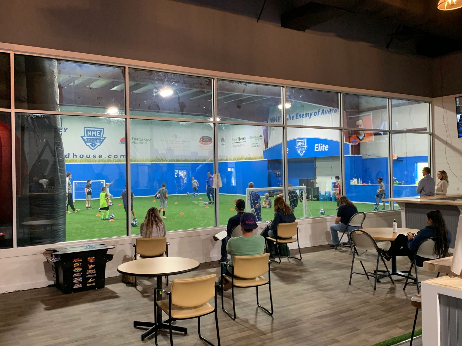 Indoor turf field with players, seen from the lounge